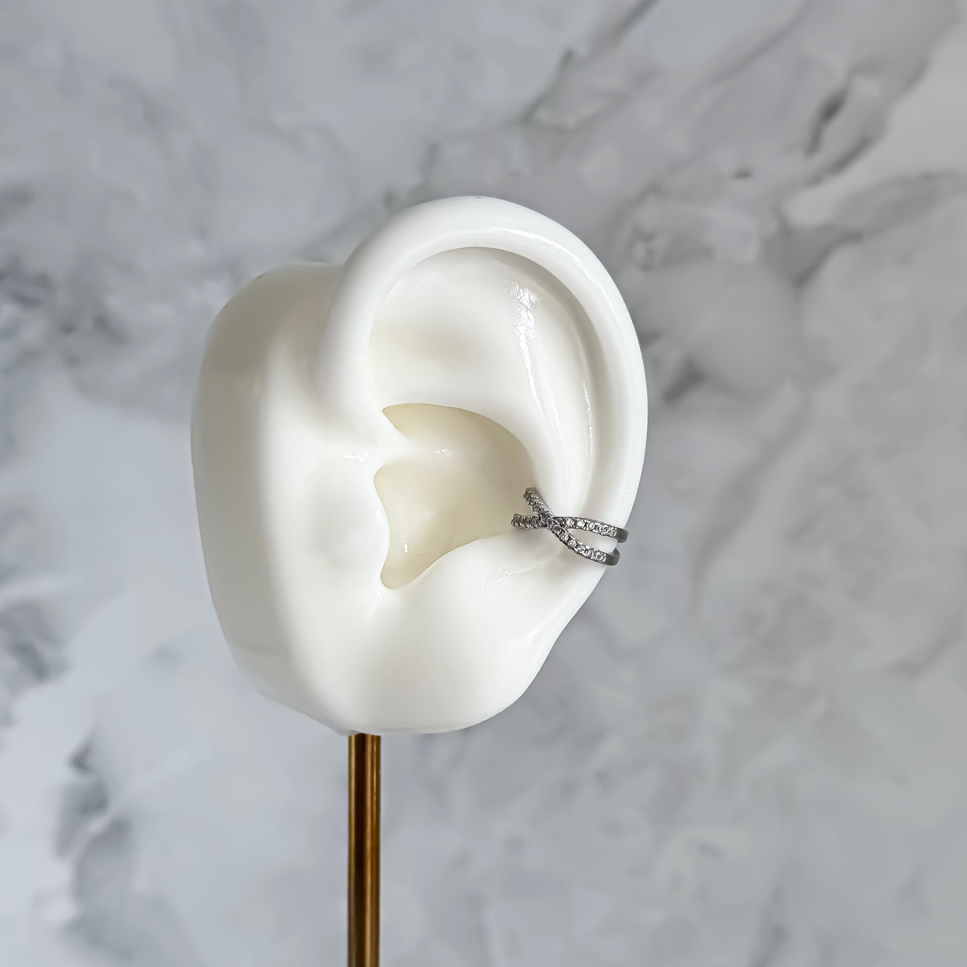 Silver ear cuff on a white ear model against a marble background