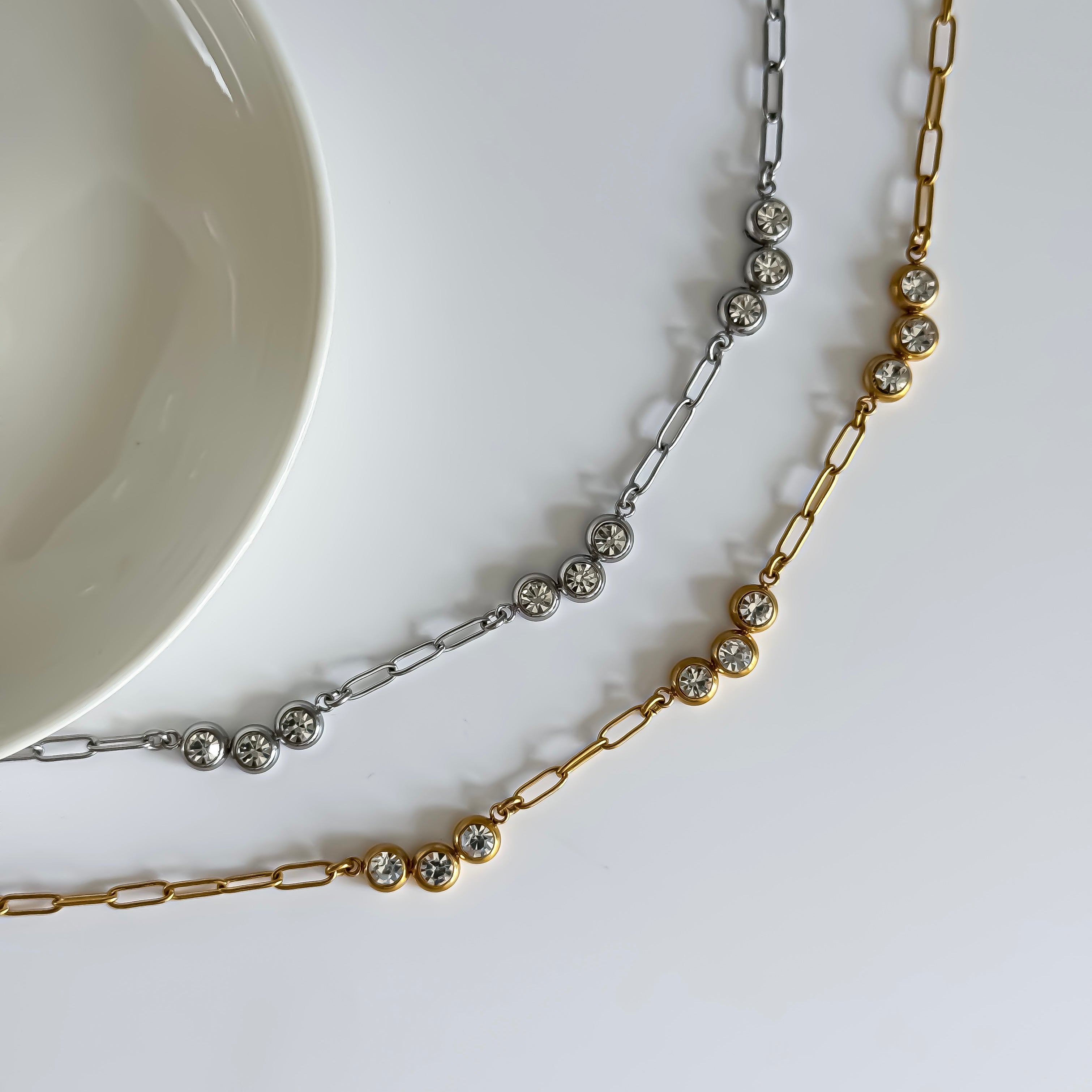 Two necklaces, one gold and one silver, with bezel-set stones on a white surface.