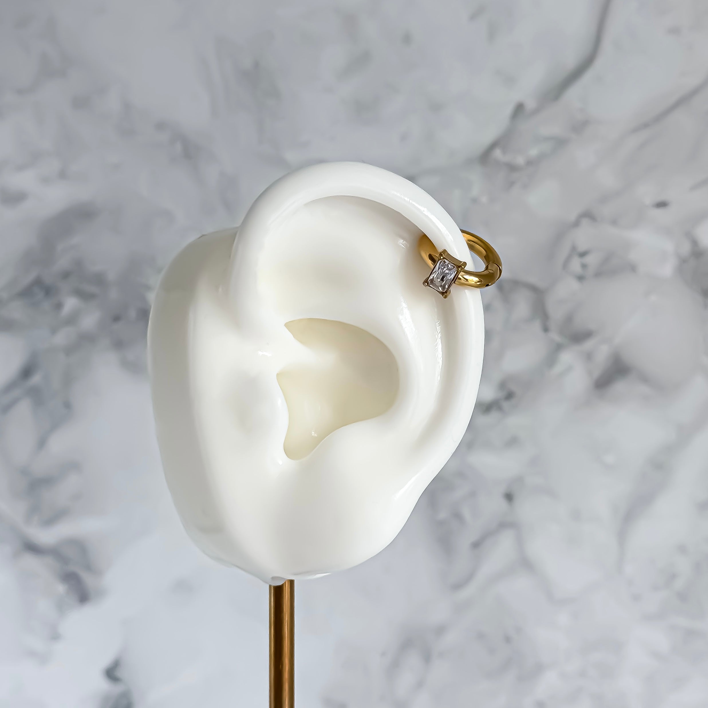 Gold ear cuff with a diamond on a white ear model against a marble background
