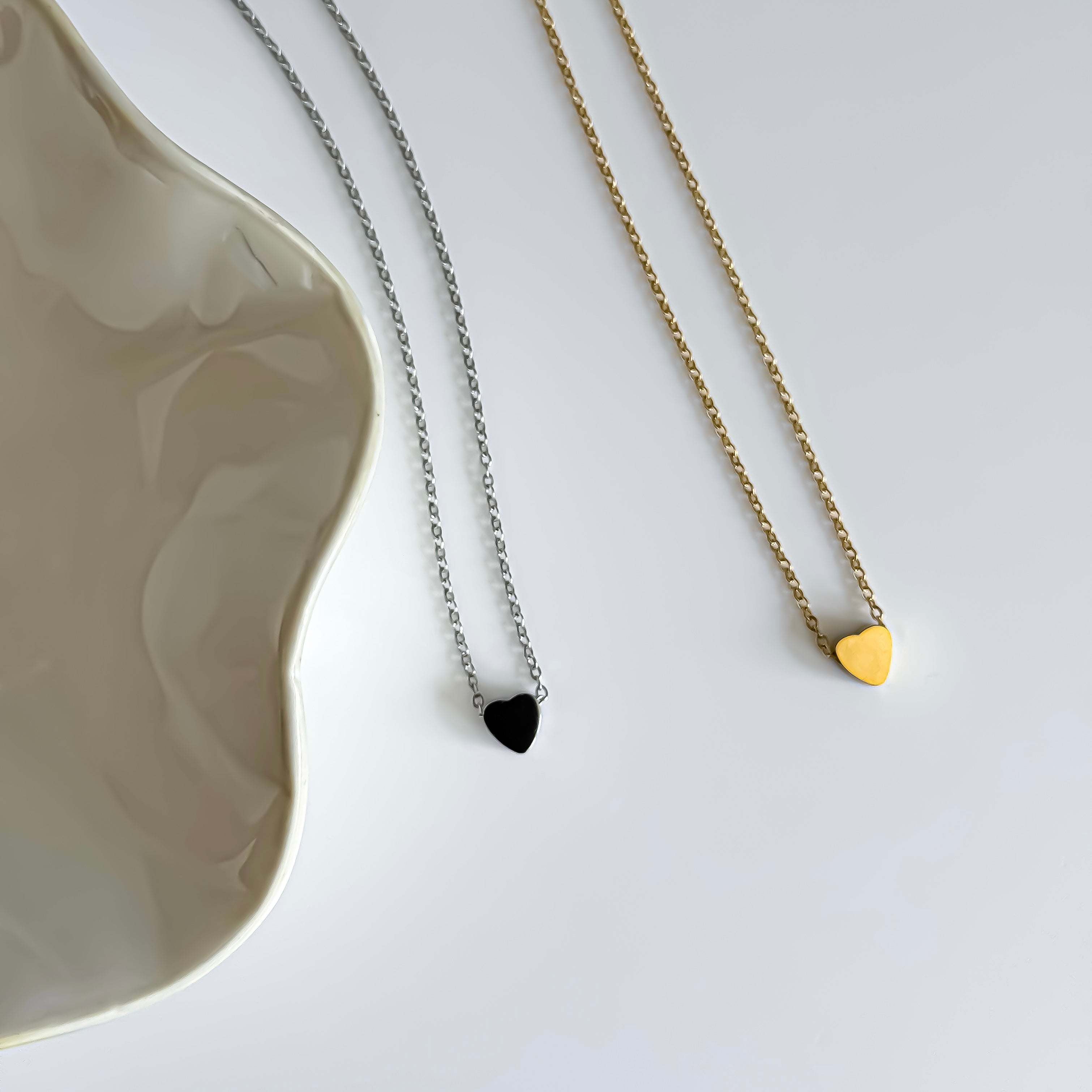 Two necklaces one gold and one silver with heart pendants on a white surface