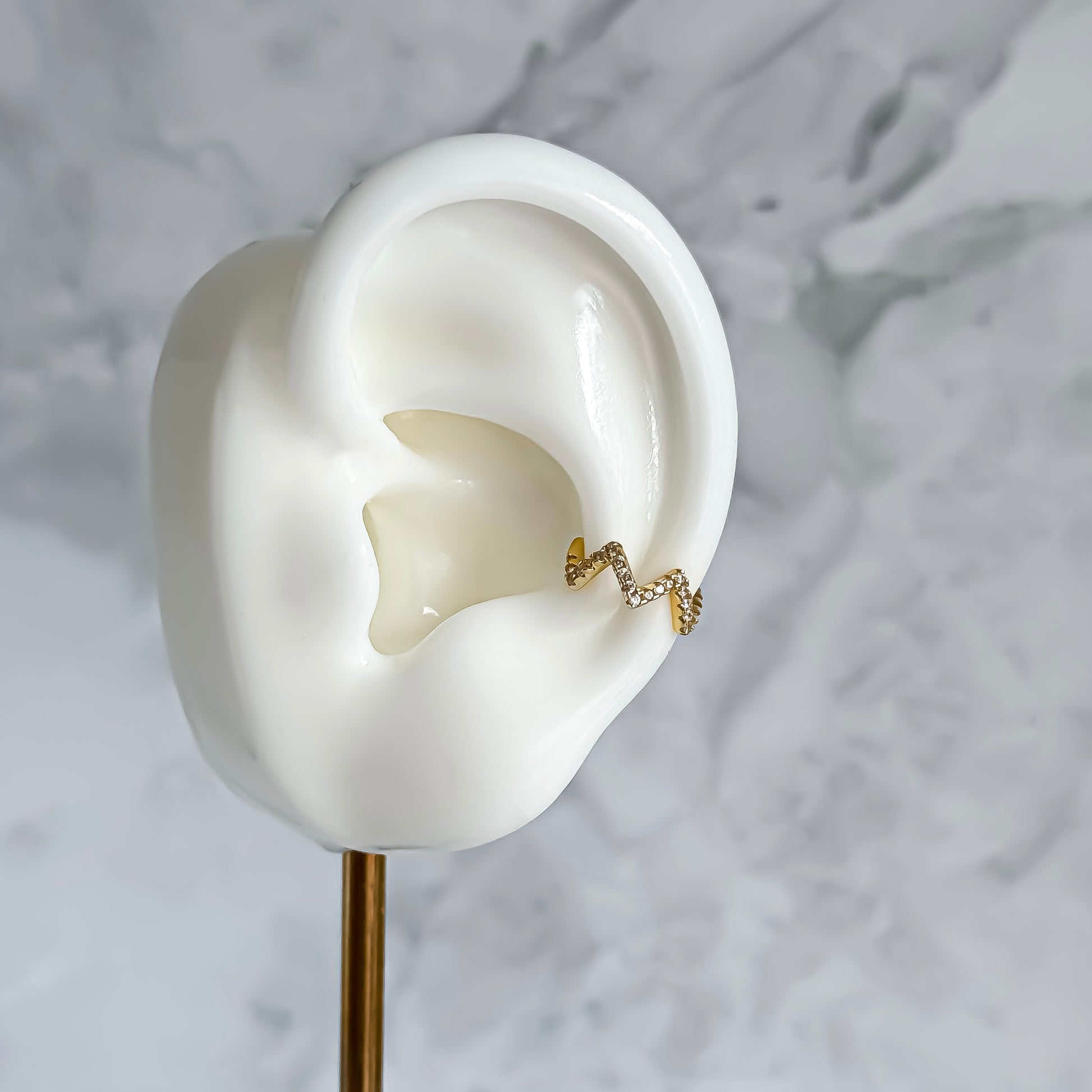 Gold ear cuff on a white ear model with a marble background