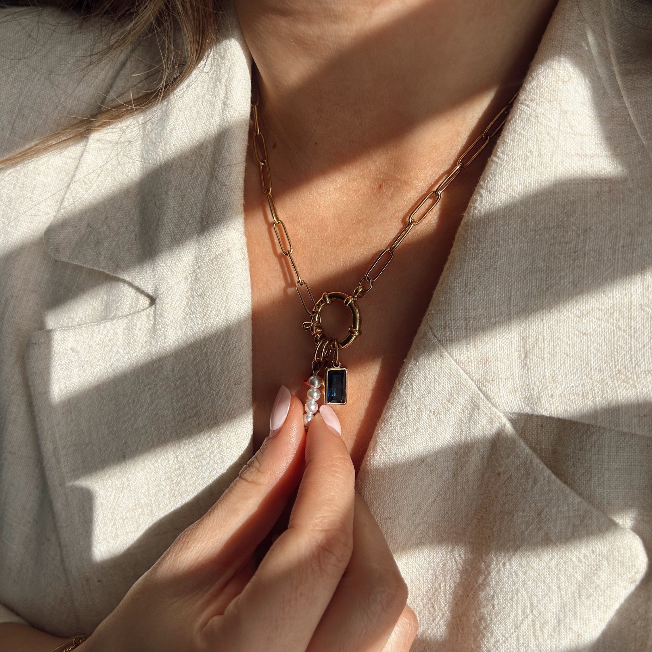 Charm Necklace with a carabiner clasp with variation of gold charms worn by a person in a light-colored outfit.