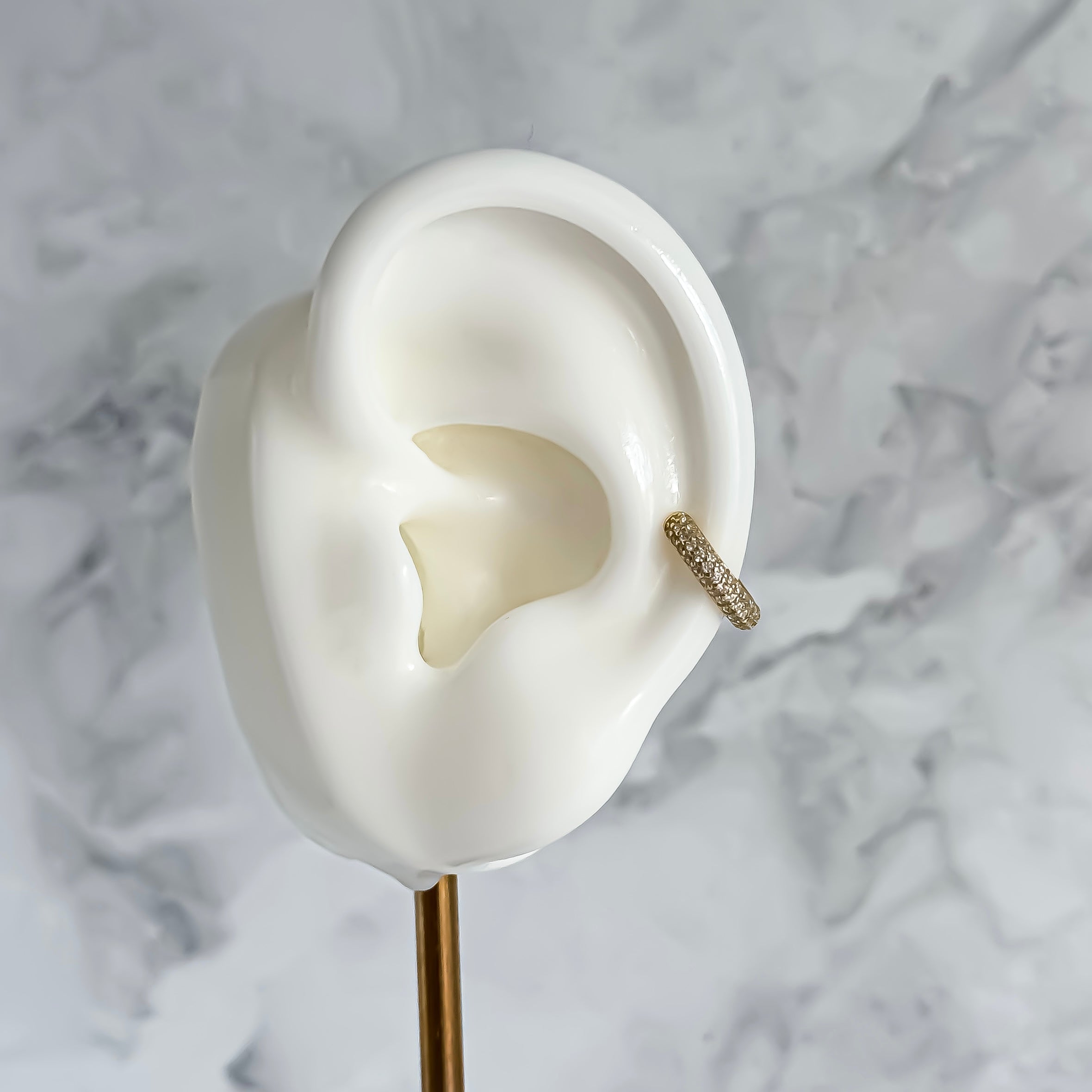 Gold ear cuff on a white ear model with a marble background