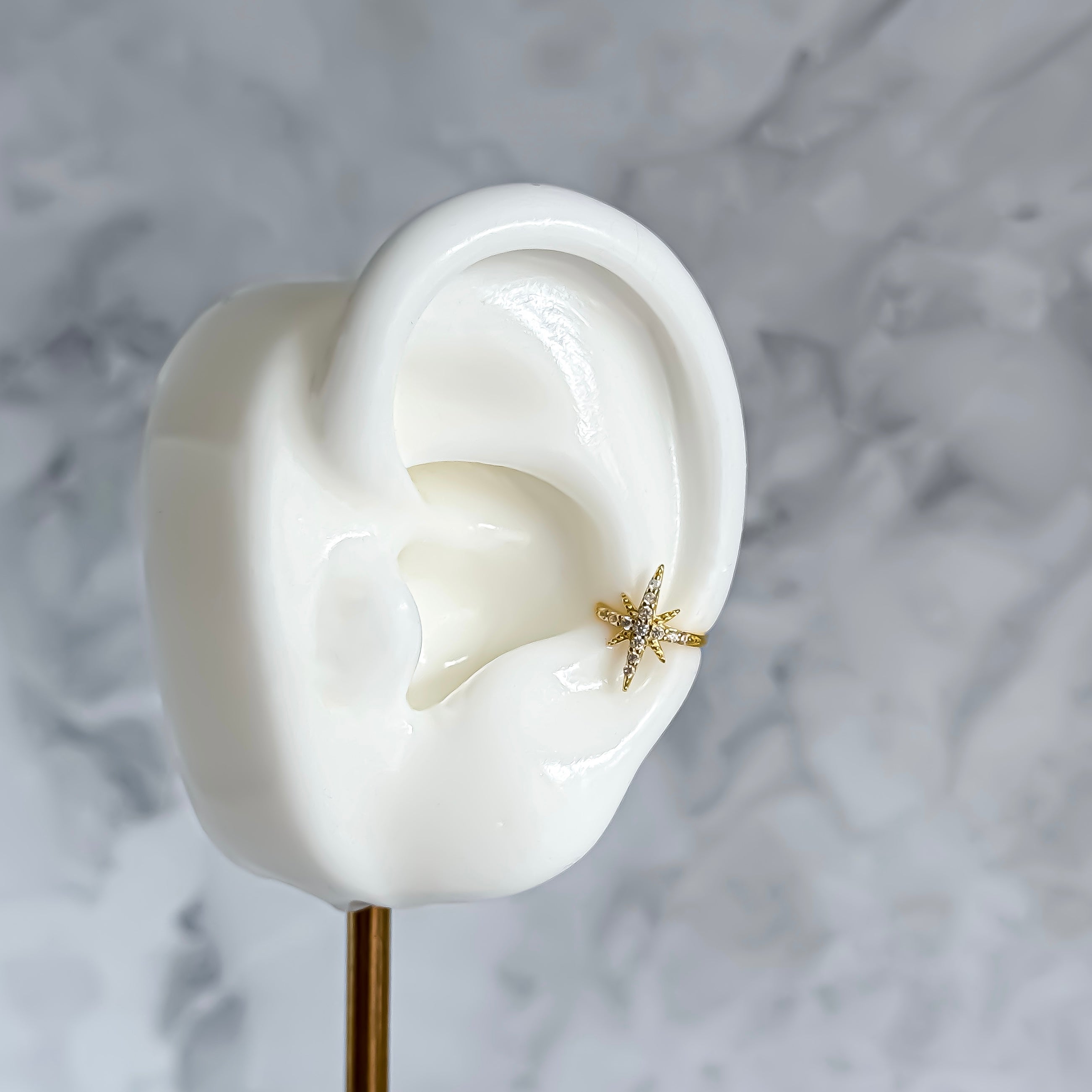Gold star-shaped ear cuff on a white ear model against a marble background