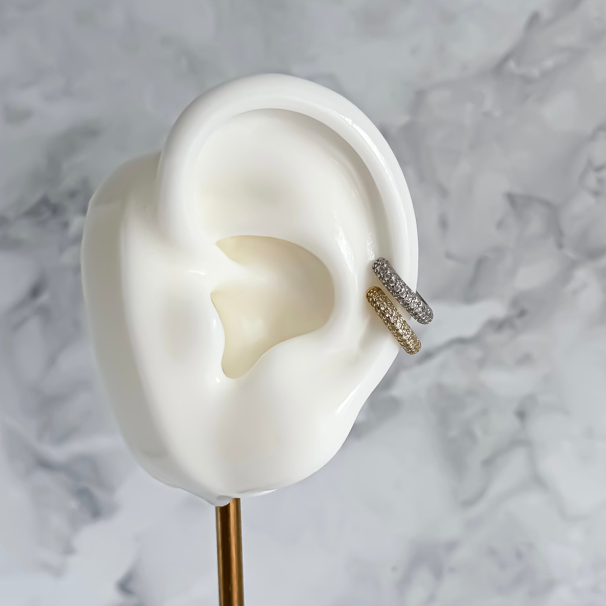 Close-up of an ear with a gold and silver ear cuff on a marble background
