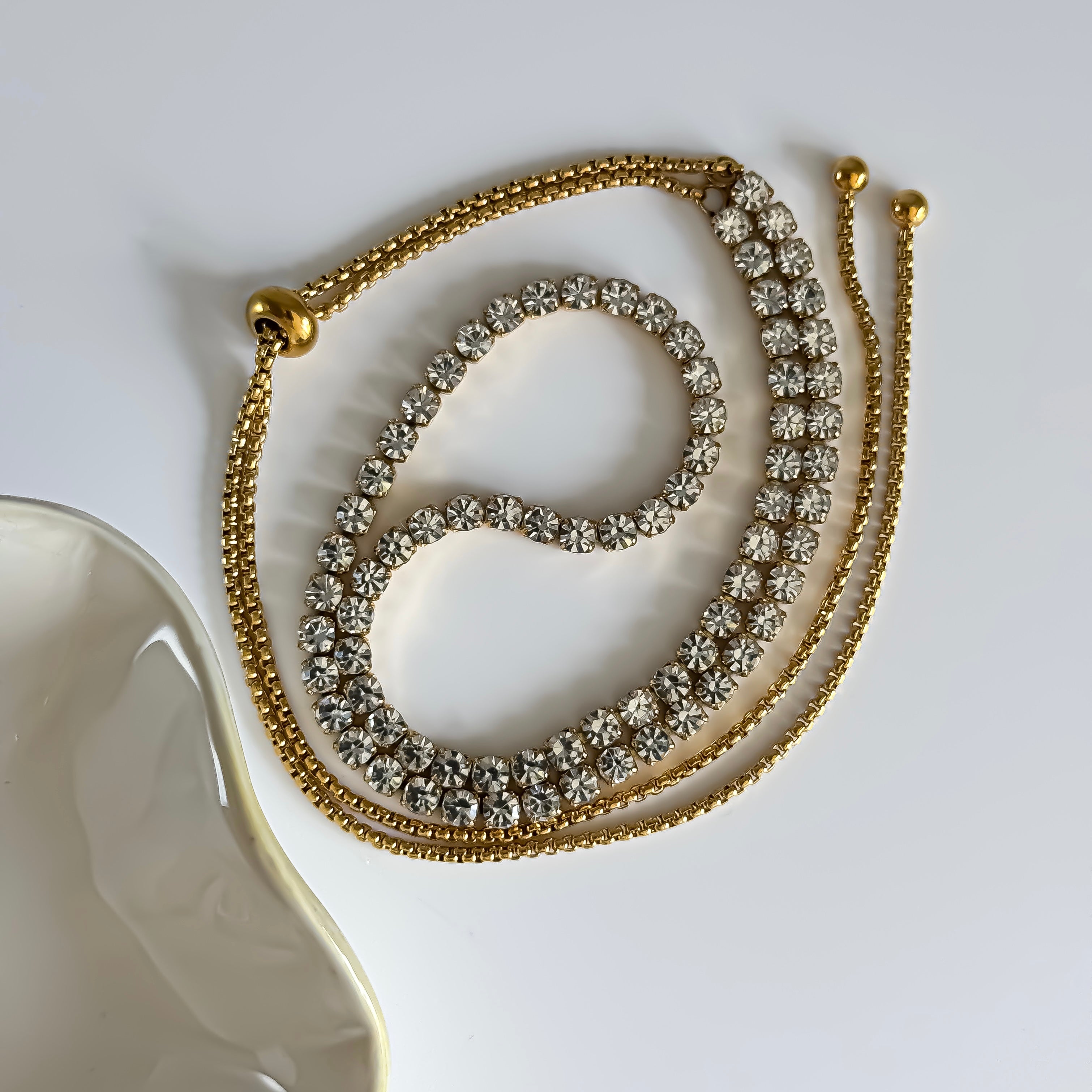 Gold tennis necklace with crystal stones on a white surface