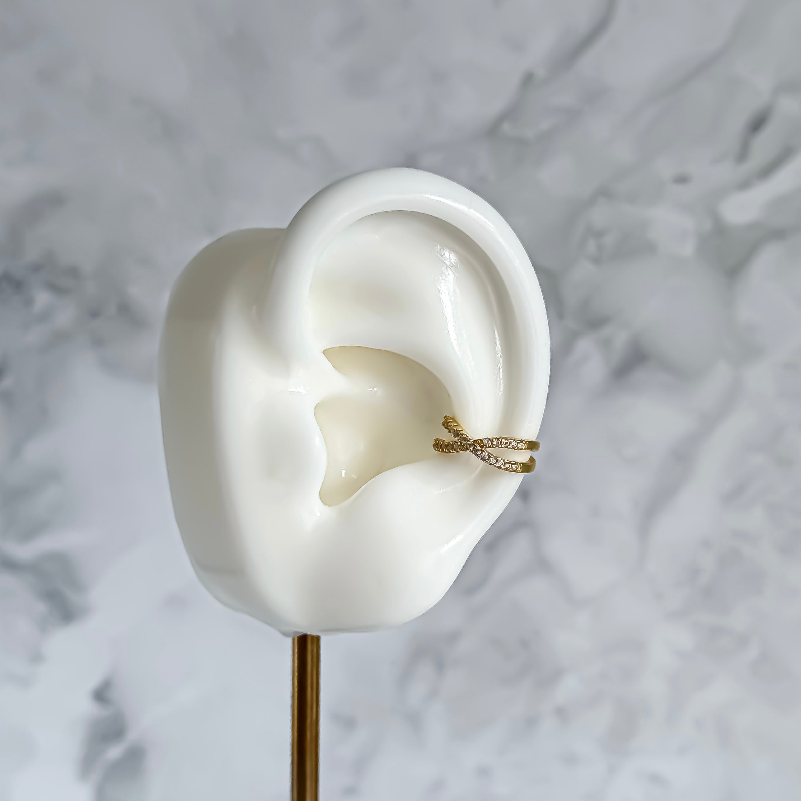 Gold ear cuff on a white ear model against a marble background