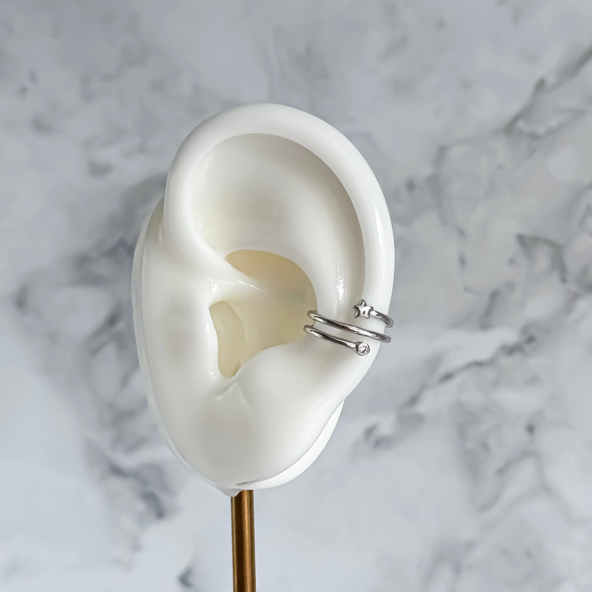 White ear model with a silver ear cuff on a marble background