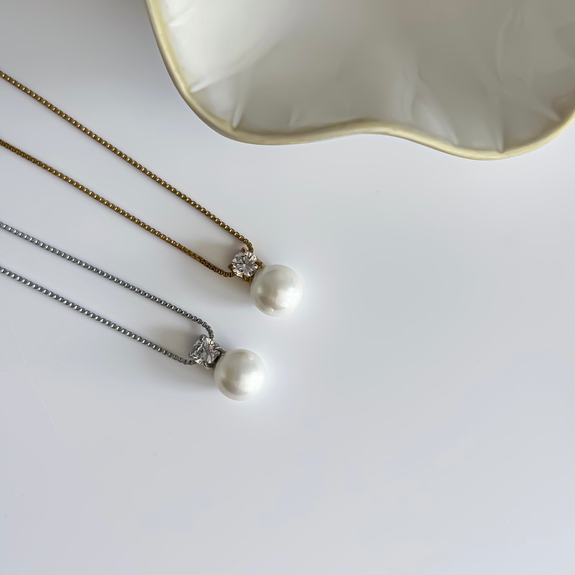 Two pearl necklaces one in gold and one in silver on a white surface