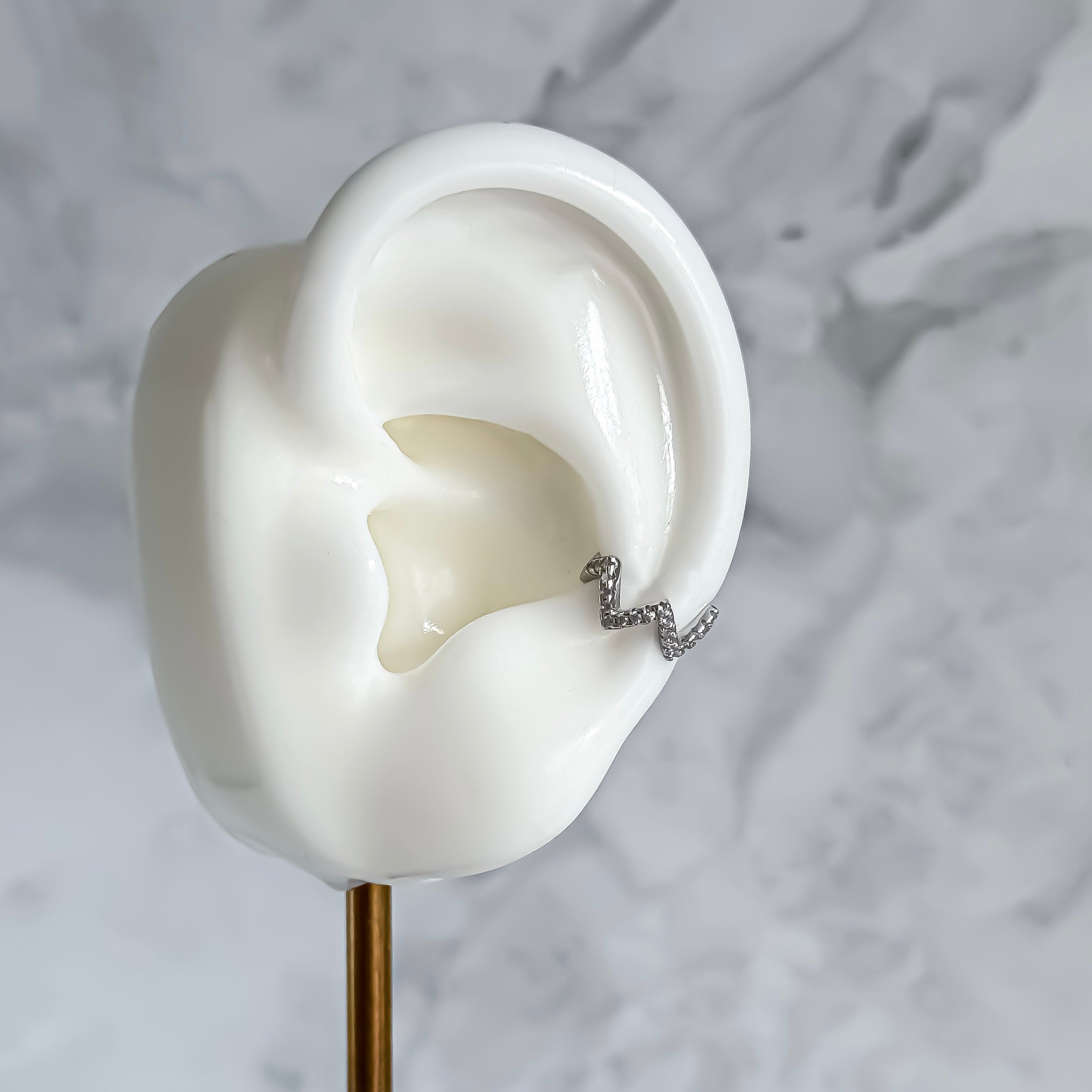 Silver ear cuff on a white ear model with a marble background