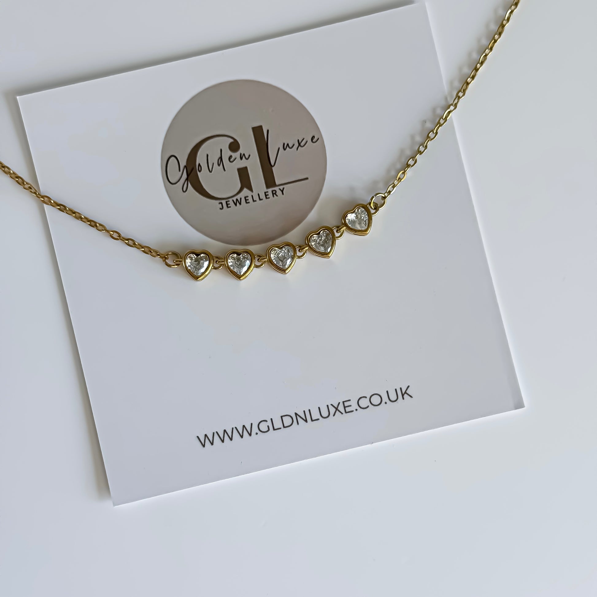 Gold necklace with heart-shaped charms on a Golden Luxe Jewellery card.