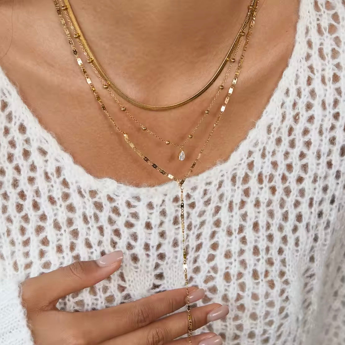 Close-up of a person wearing a gold layered necklace with a white lace top.