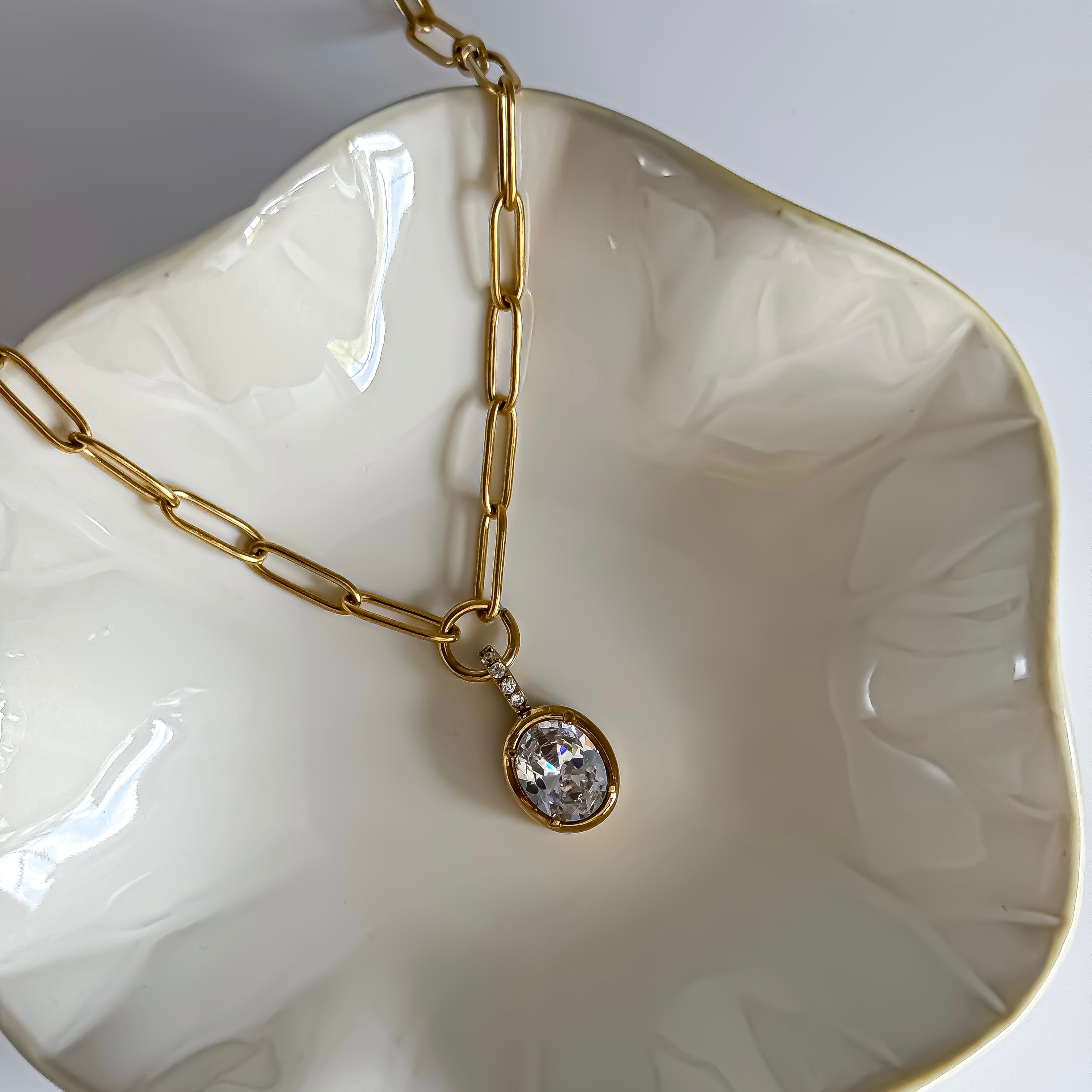 Gold chain necklace with a pendant on a white dish