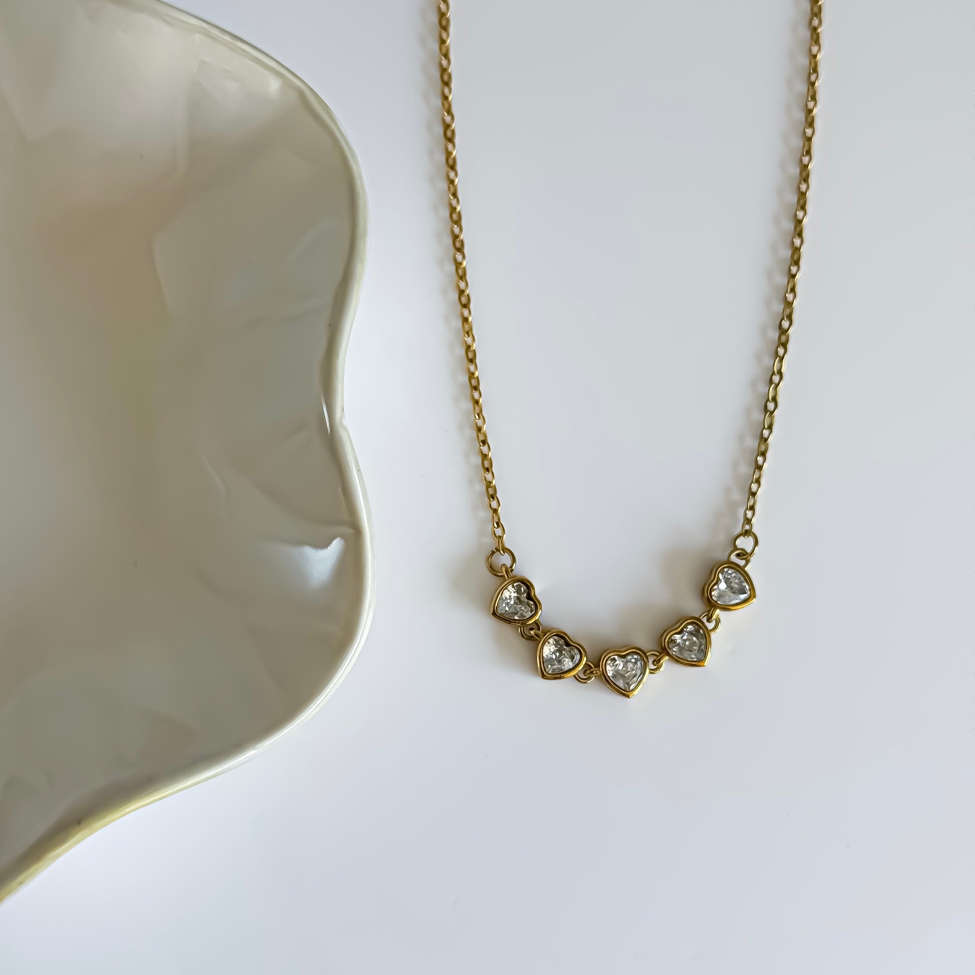 Gold necklace with heart-shaped gemstones on a white surface
