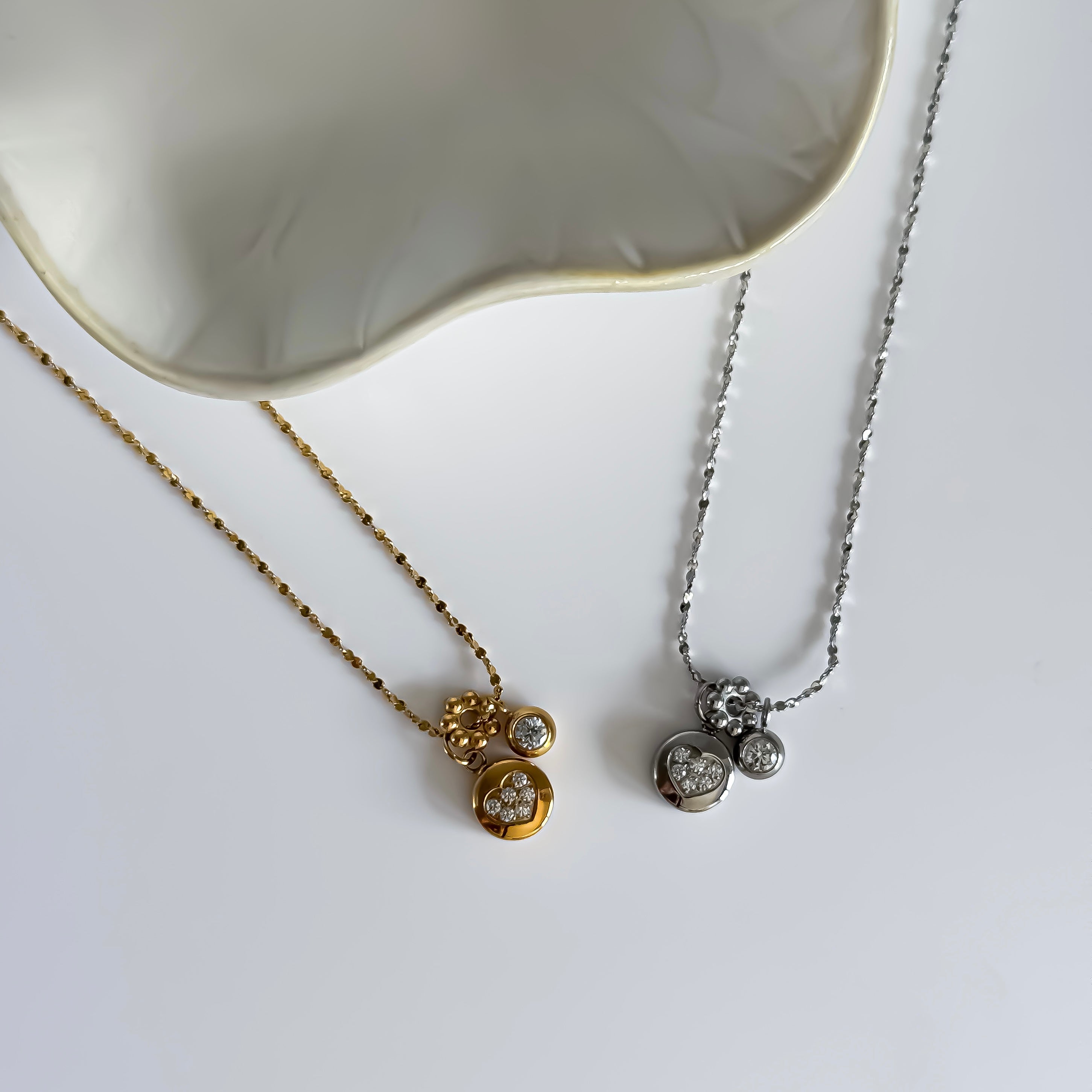 Two necklaces with diamond pendants on a white surface.