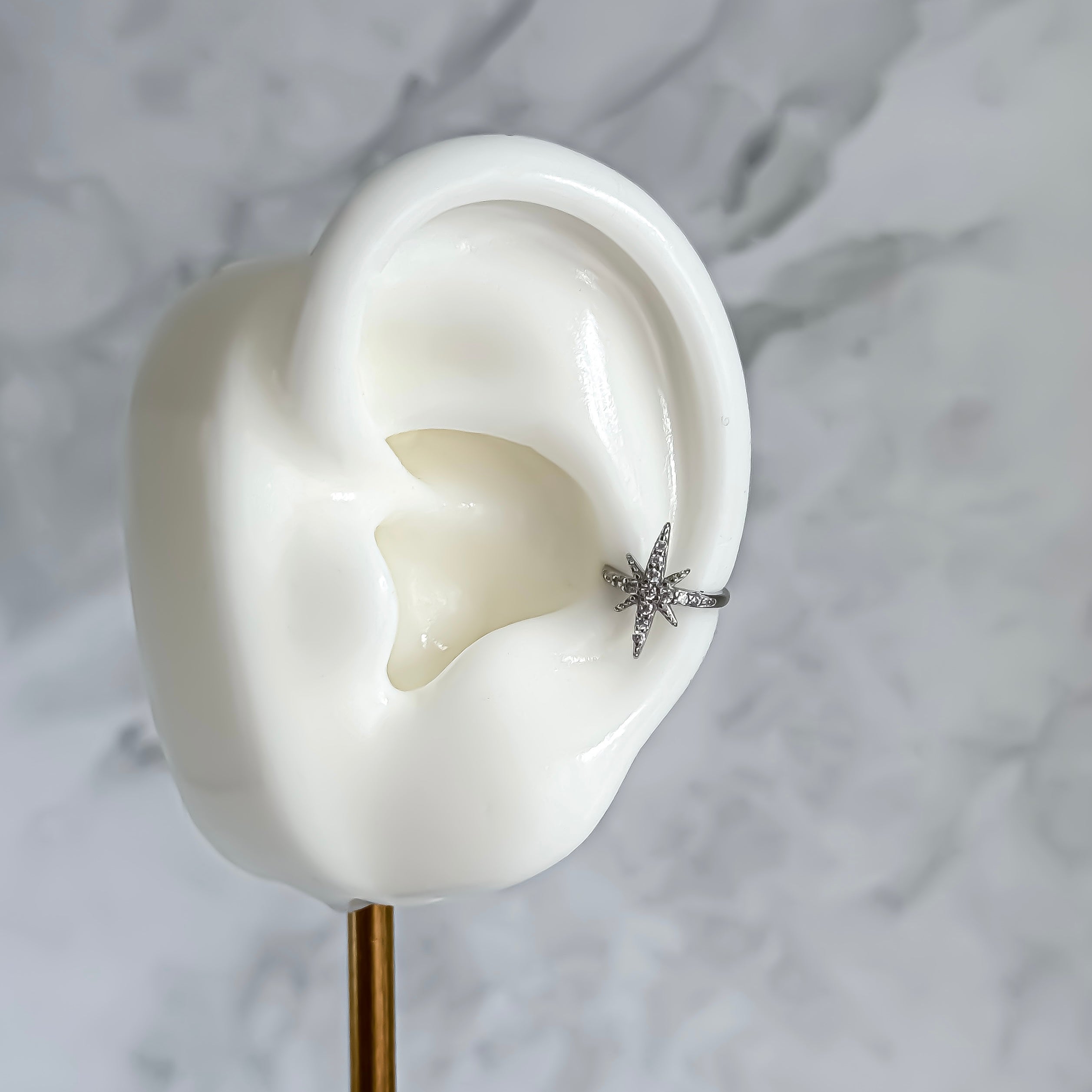 Silver star-shaped ear cuff on a white ear model with a marble background