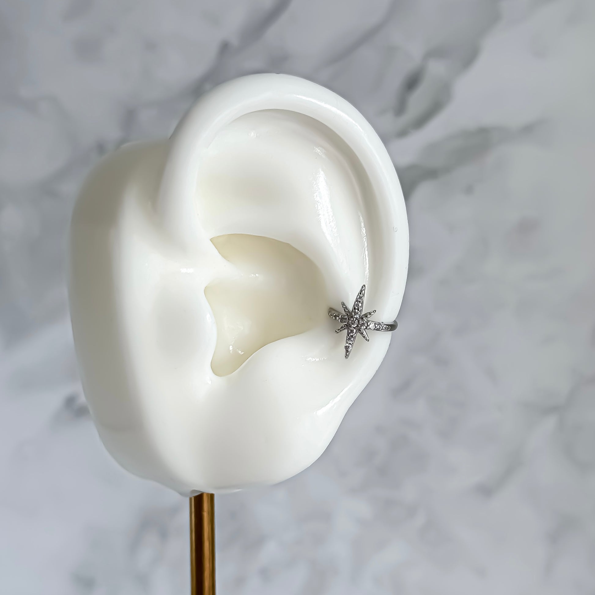Silver star-shaped ear cuff on a white ear model with a marble background