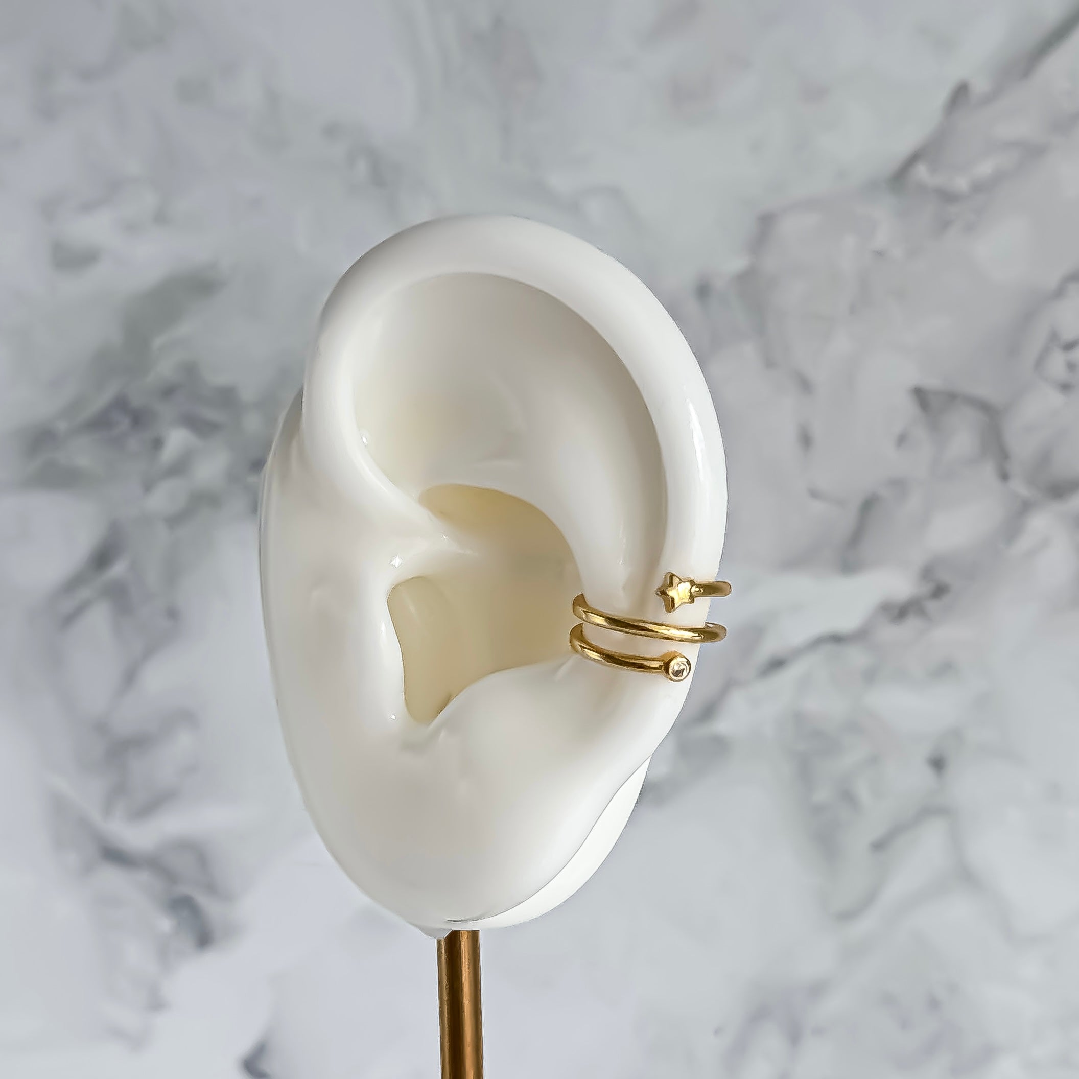 Gold ear cuff on a white ear model against a marble background