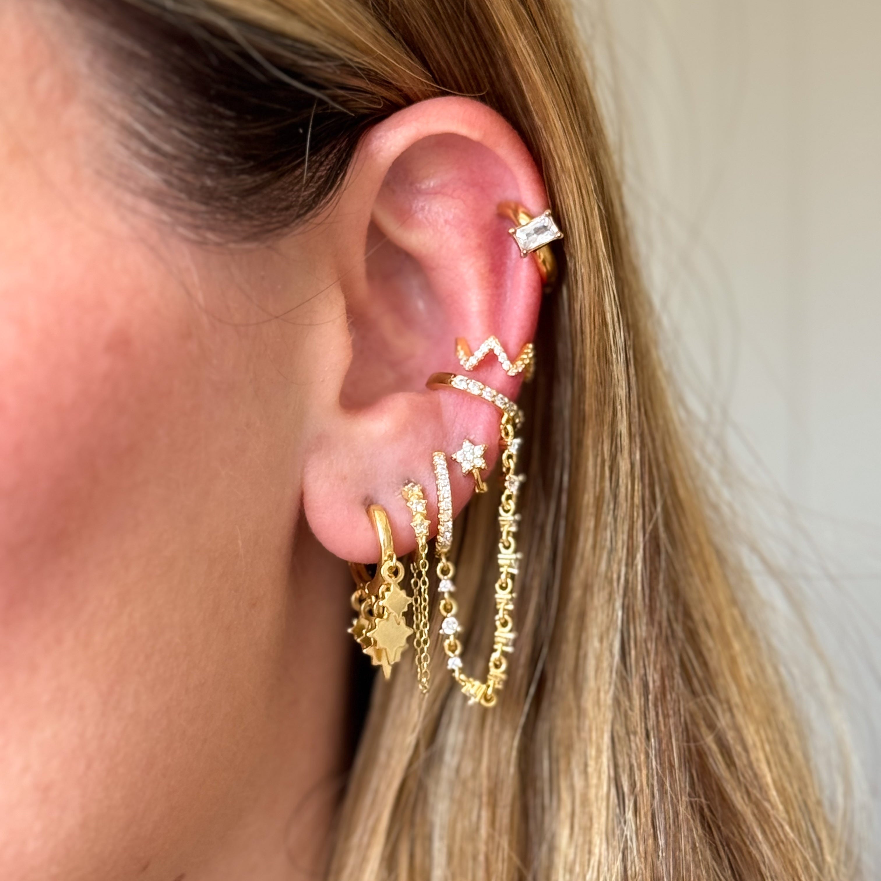 Close-up of an ear with multiple gold earrings on a neutral background