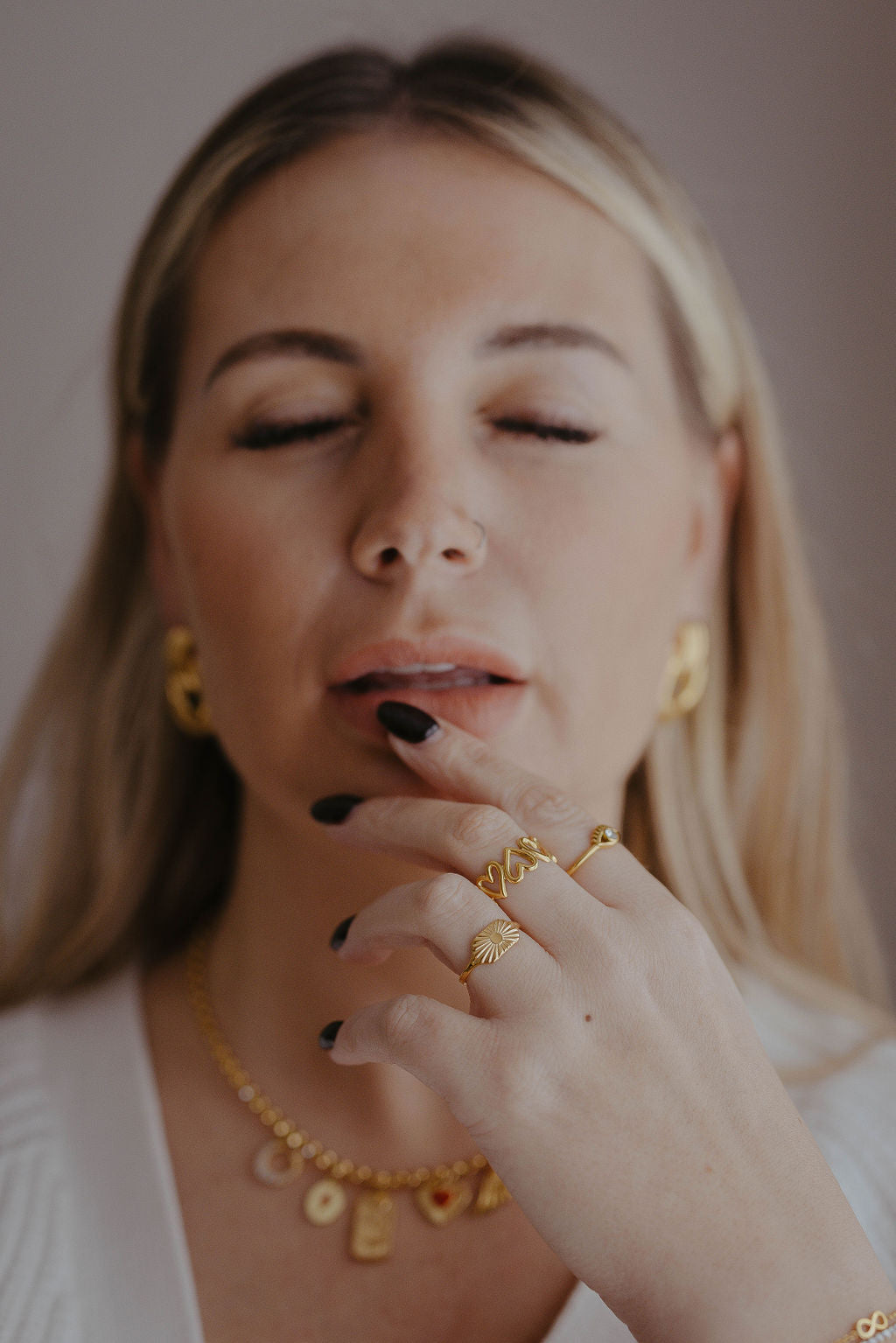 Woman wearing gold jewelry including earrings, necklace, and ring against a neutral background