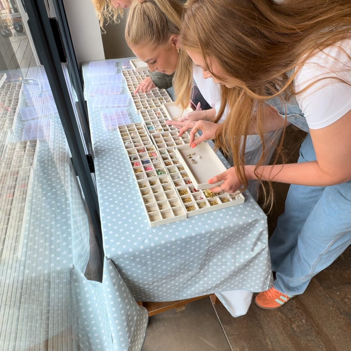 Two women looking at a tray of small charms in a cafe setting.