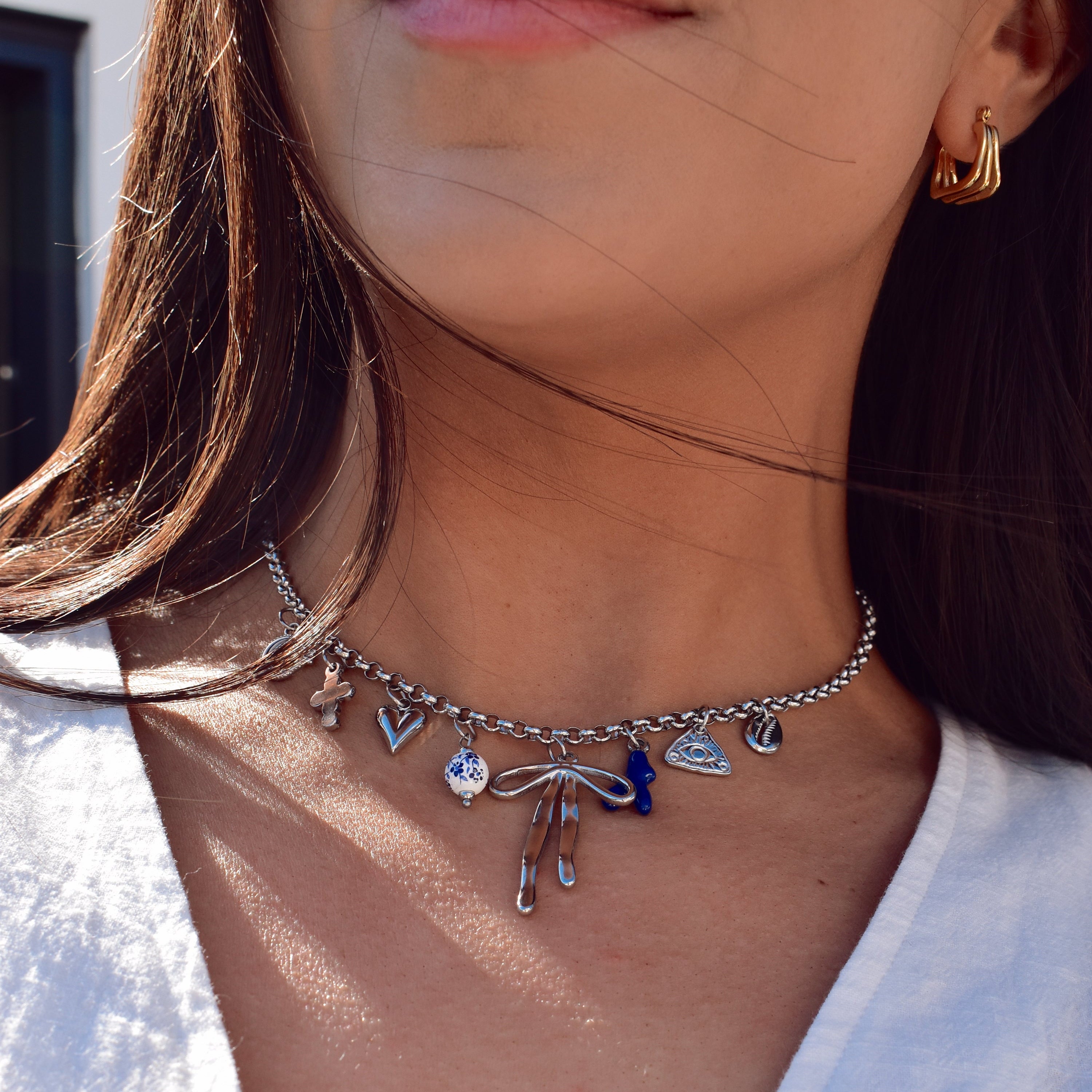 Close up of model wearing silver charm necklace with a mixed variation of silver charms, paired with a small gold hoop earring