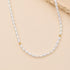 A delicate necklace made of small white baroque pearls with small gold spacer beads, displayed on a beige background with a textured stone prop.