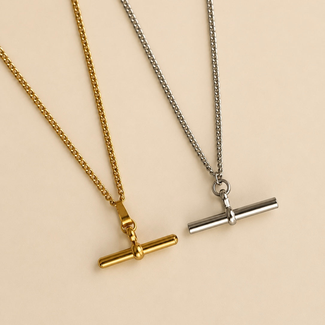 Two minimalist toggle bar necklaces, one in polished gold and one in silver, displayed on a warm beige background.