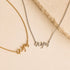 Two name necklaces with cursive script pendants, one in gold and one in silver, displayed on a light beige background with a textured stone prop.