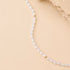 A delicate strand of white baroque pearls separated by small gold spacer beads, laid out on a warm beige background with a textured stone prop in the top right corner.